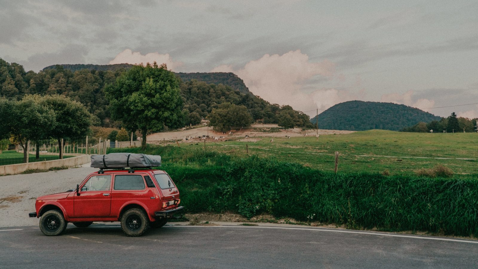 Red car parked by green hills